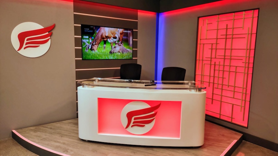 High school TV production studio set with custom anchor desk, studio lighting, broadcast display, and branded backdrop