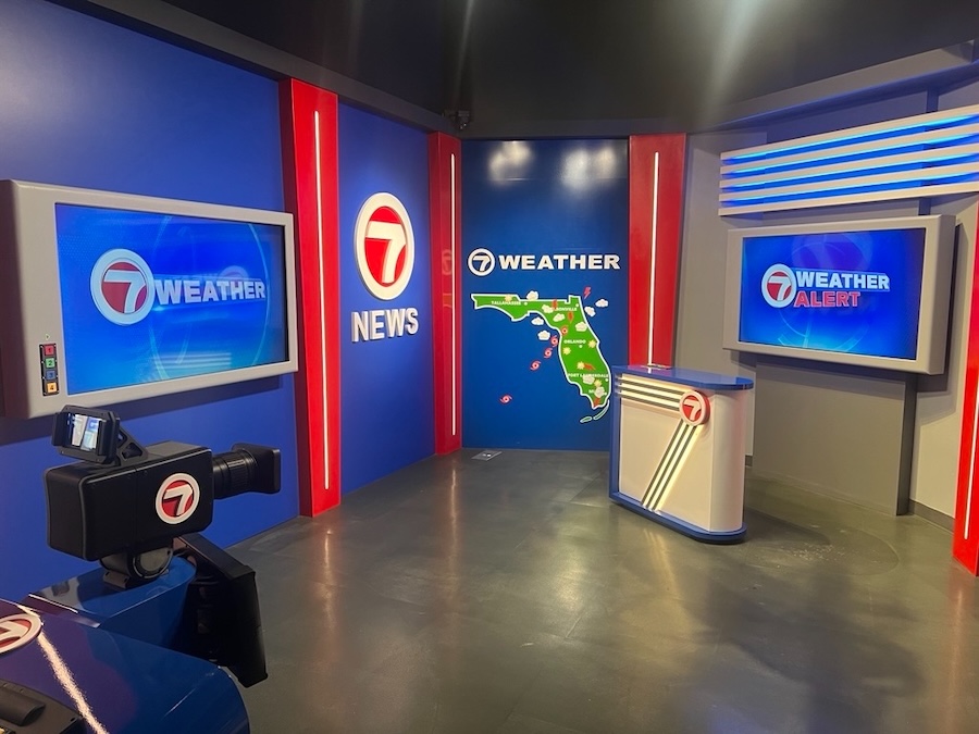 Interactive weather studio exhibit with broadcast cameras, weather graphics, and a news-style set at a science museum