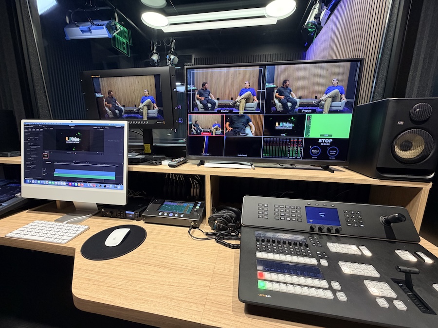 Broadcast control room with multi-view monitors, custom shallow console, and professional audio mixing equipment.